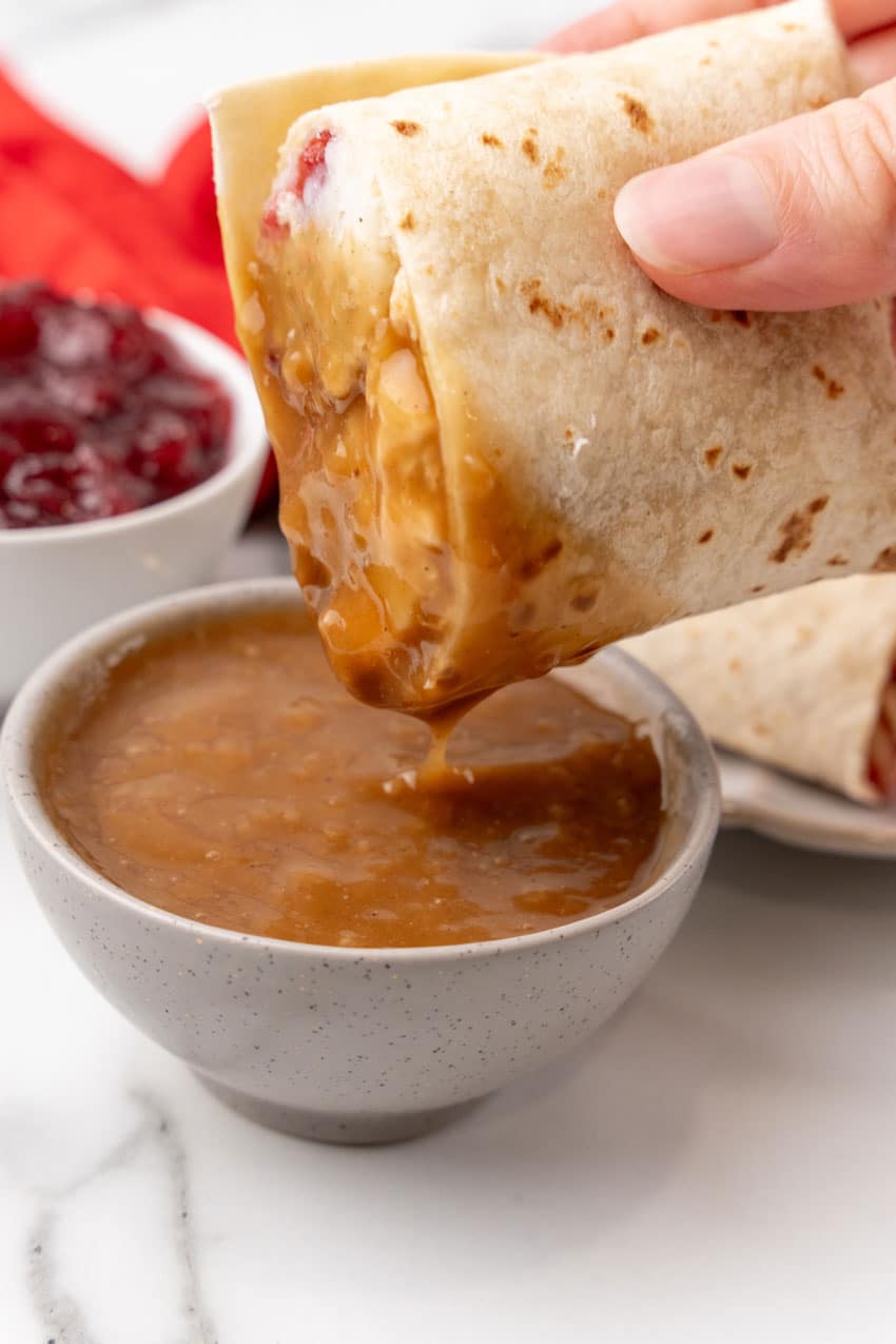 a hand holding up half of a leftover turkey burrito that's been dipped in brown gravy