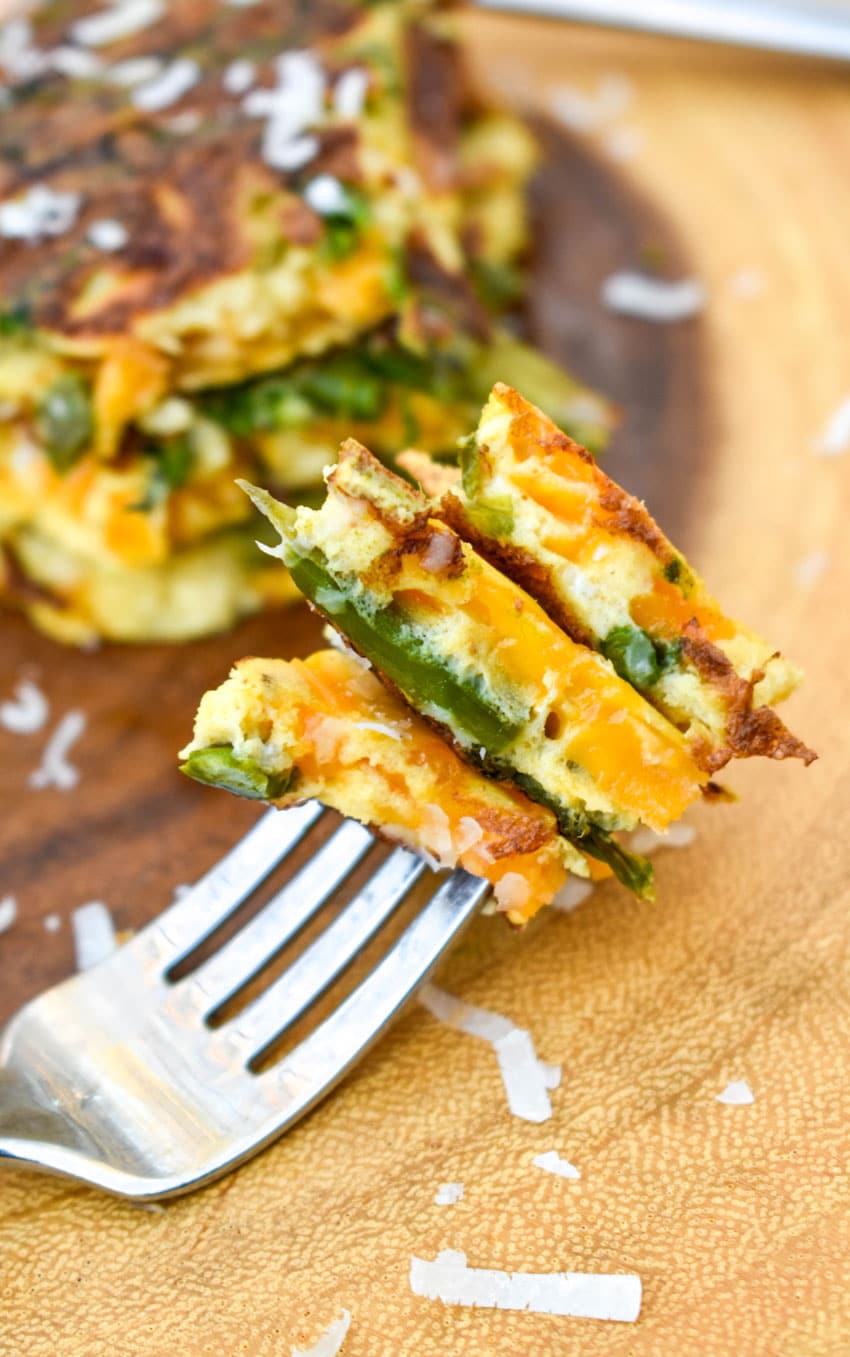 a silver fork holding bites of cheddar asparagus frittata resting on a wooden cutting board