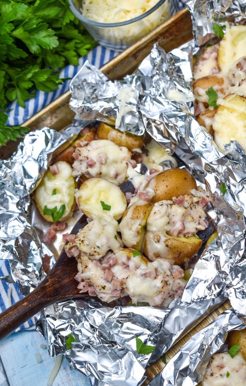 a wooden spatula scooping cheesy chicken cordon bleu and potatoes out of a foil packet