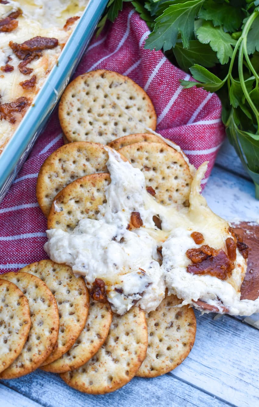 a pile of crackers topped with creamy caesar dip with bacon resting on a red cloth napkin