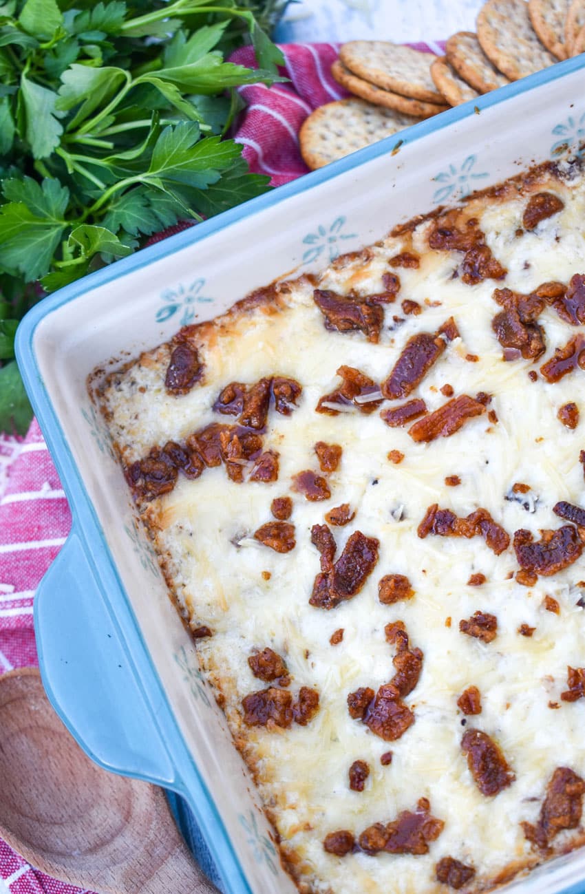 creamy caesar dip with bacon in a blue square baking dish