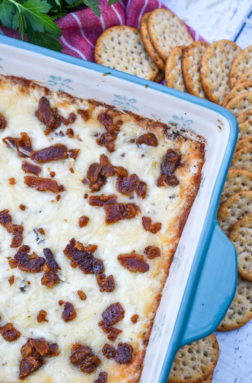 creamy caesar dip with bacon in a blue square baking dish