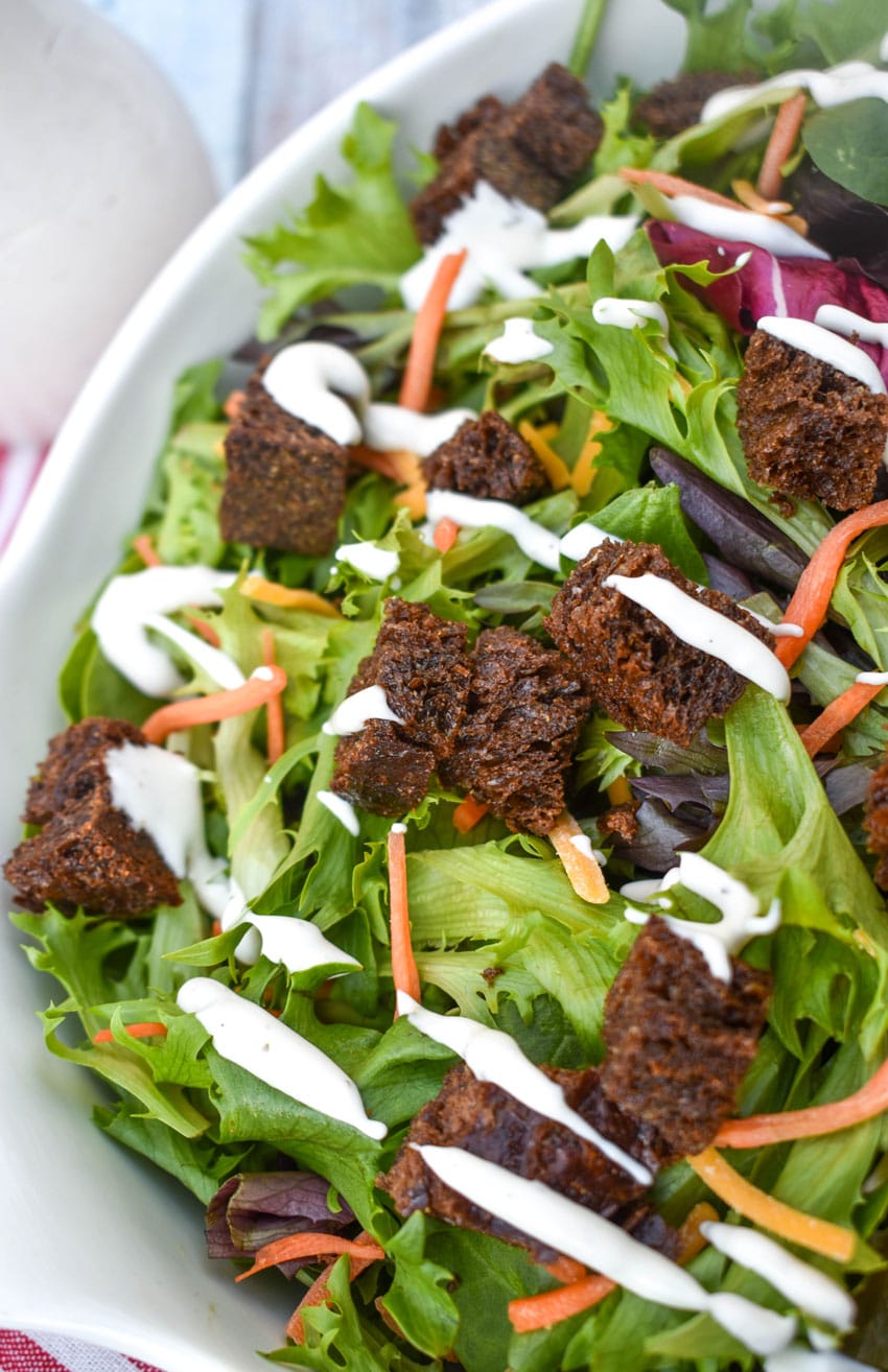 PUMPERNICKEL CROUTONS ON A GREEN SALAD IN A WHITE SERVING BOWL