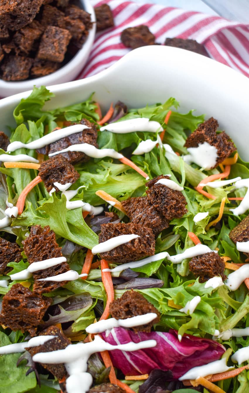 PUMPERNICKEL CROUTONS ON A GREEN SALAD IN A WHITE SERVING BOWL