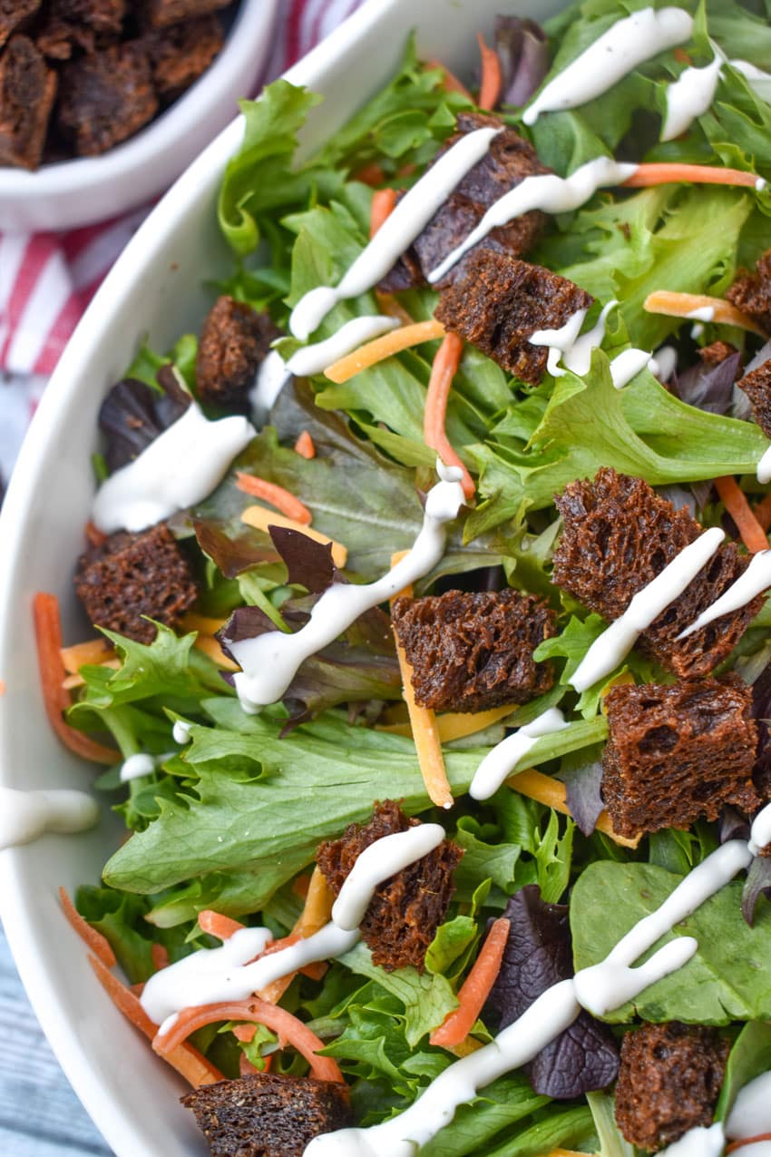 PUMPERNICKEL CROUTONS ON A GREEN SALAD IN A WHITE SERVING BOWL