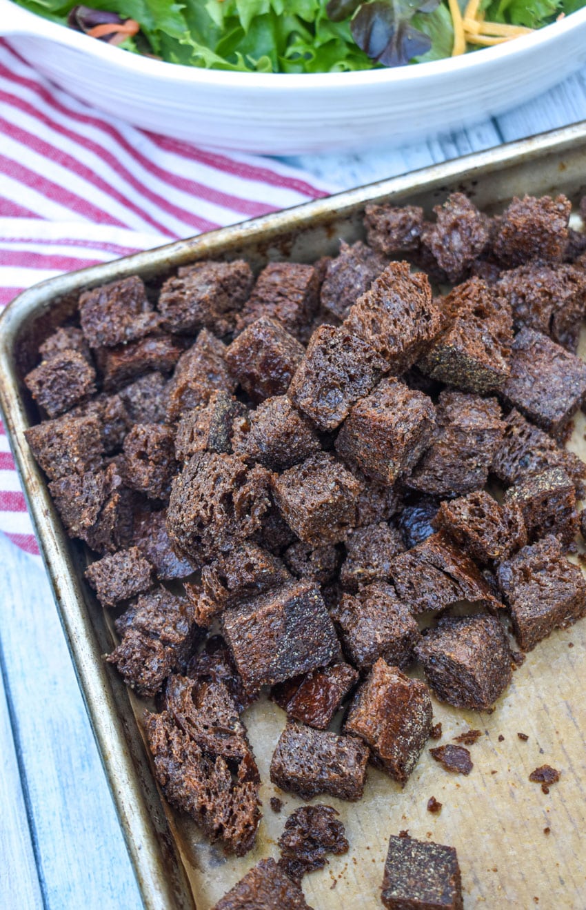 PUMPERNICKEL CROUTONS ON A BROWN PARCHMENT PAPER LINED BAKING SHEET