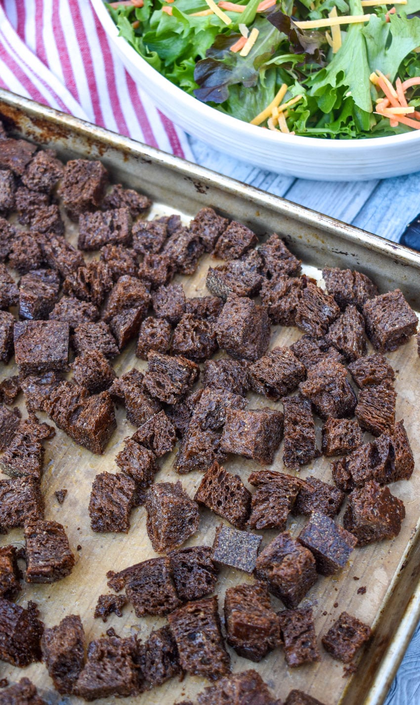 PUMPERNICKEL CROUTONS ON A BROWN PARCHMENT PAPER LINED BAKING SHEET