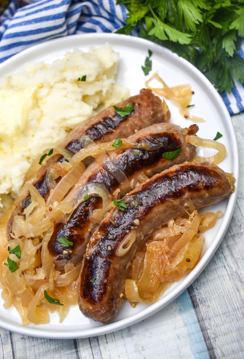 slow cooker bratwurst and sauerkraut on a white plate with mashed potatoes on the side