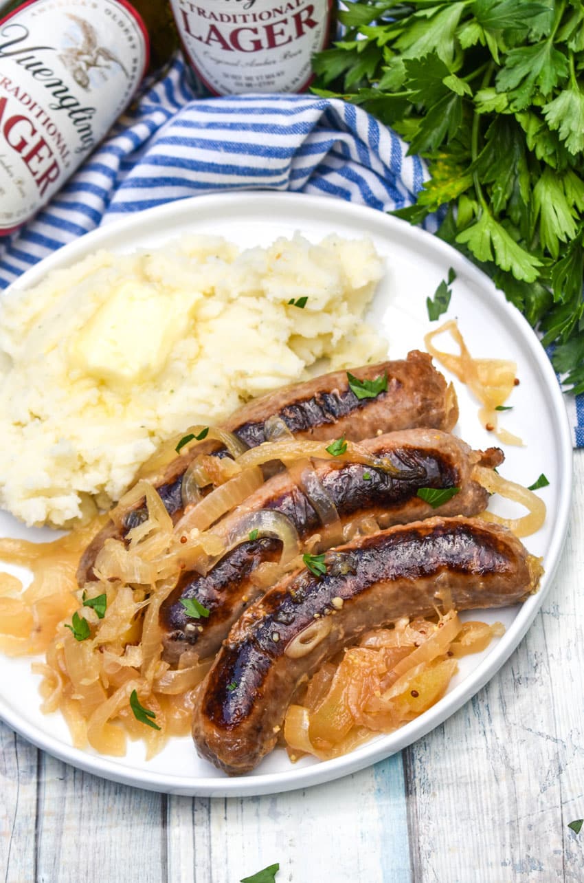 slow cooker bratwurst and sauerkraut on a white plate with mashed potatoes on the side