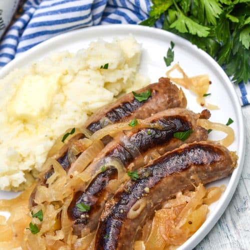 slow cooker bratwurst and sauerkraut on a white plate with mashed potatoes on the side