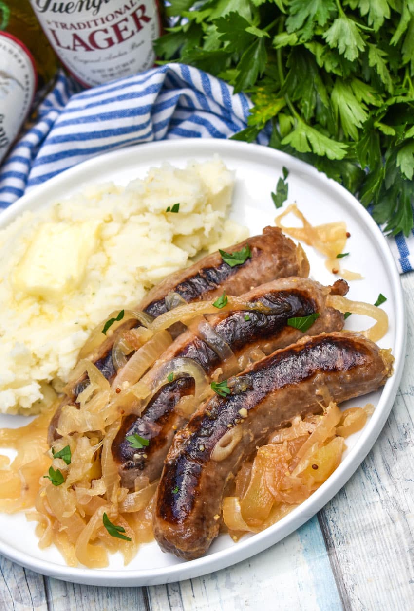 slow cooker bratwurst and sauerkraut next to mashed potatoes on a white plate