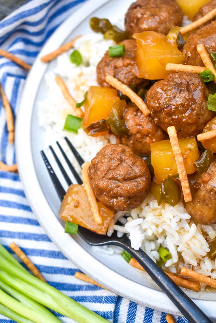 crockpot hawaiian meatballs over steamed white rice on a white dinner plate with a black fork resting on the side