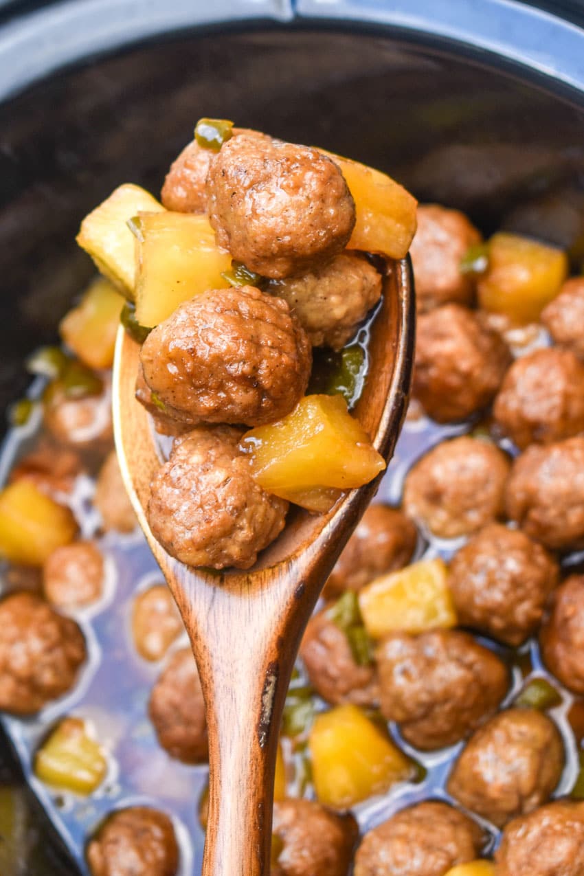 a wooden spoon holding up a scoop of crockpot hawaiian meatballs