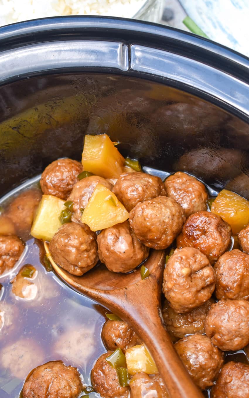 a wooden spoon scooping hawaiian meatballs out of a black crock