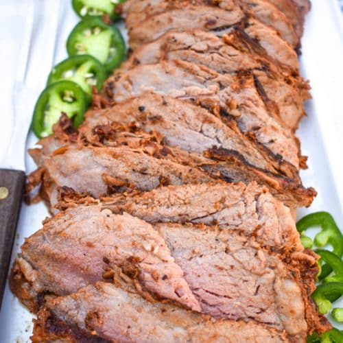 slices of smoked tri tip arranged in a row on a white serving platter