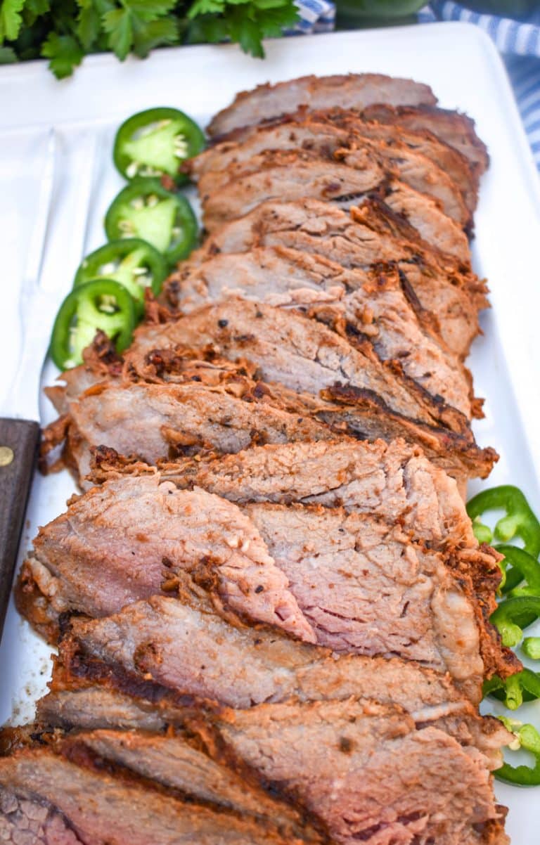 slices of smoked tri tip arranged in a row on a white serving platter