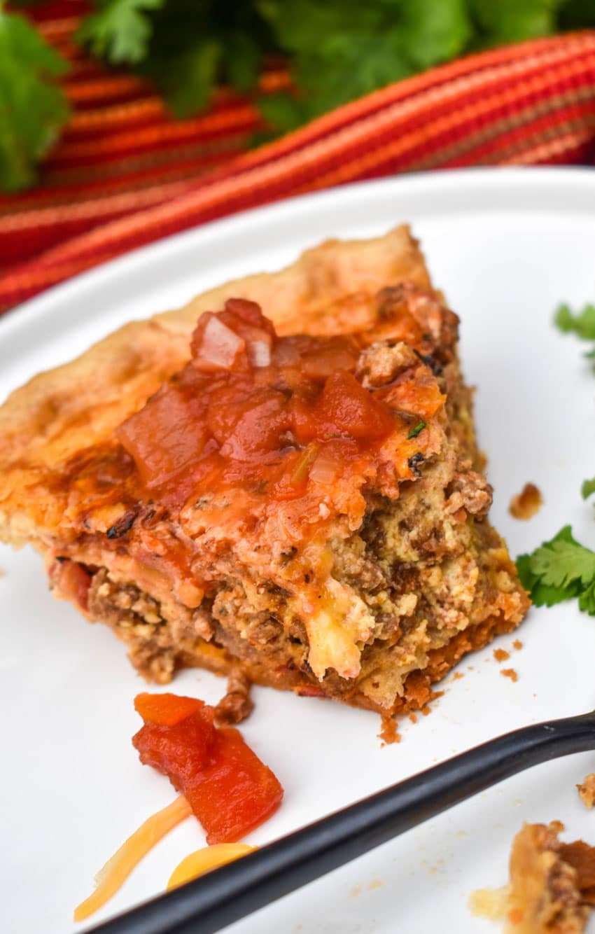 A SLICE OF A SOUTHWESTERN QUICHE TOPPED WITH SALSA ON A WHITE DINNER PLATE