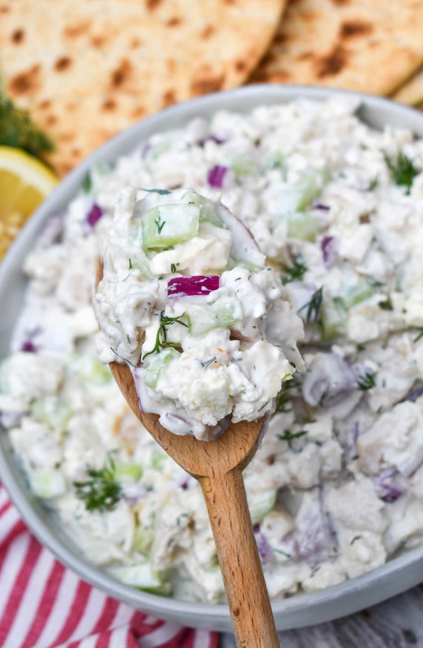 a wooden spoon holding up a scoop of tzatziki chicken salad