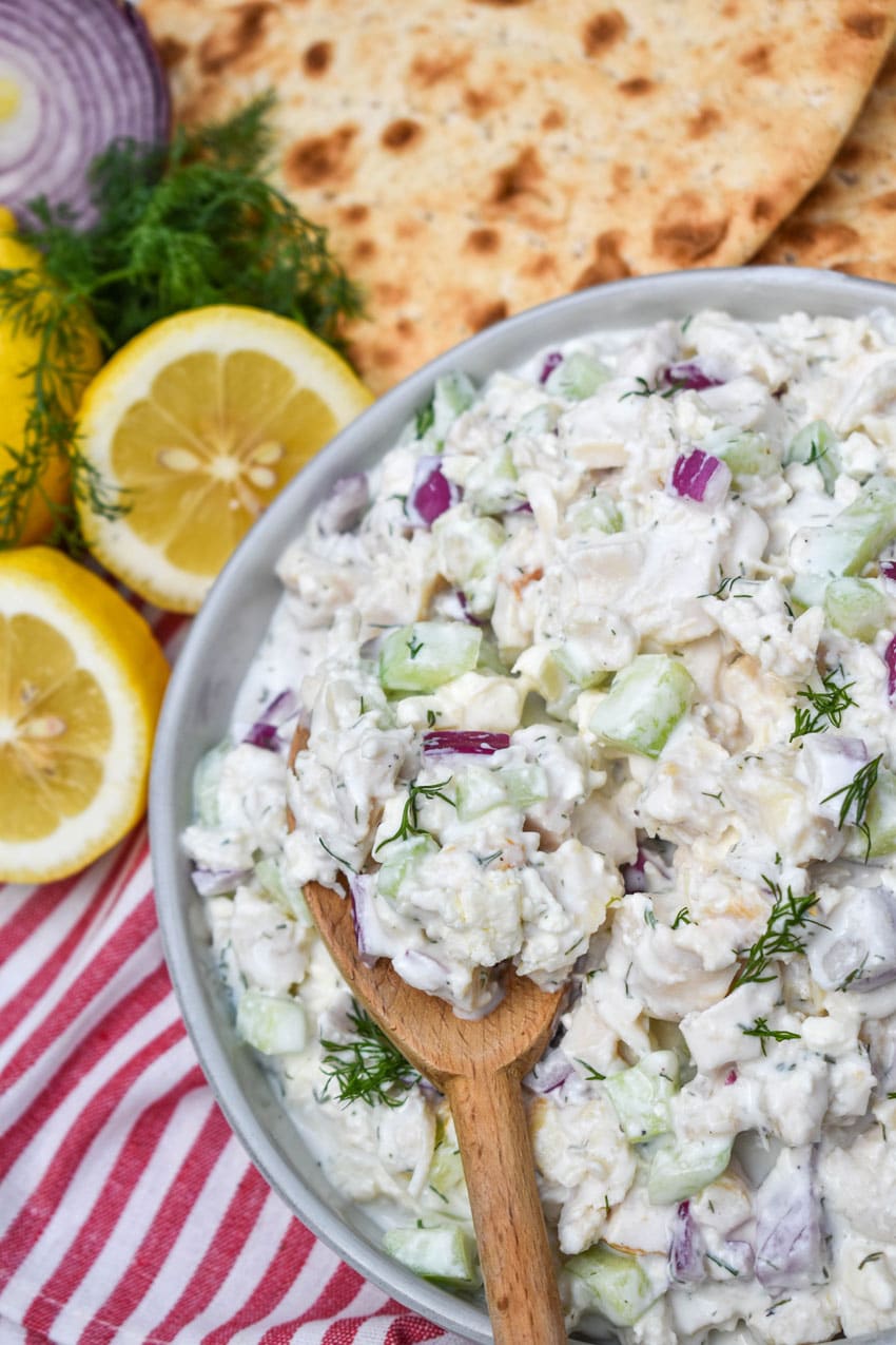 a wooden spoon scooping tzatziki chicken salad out of a gray bowl