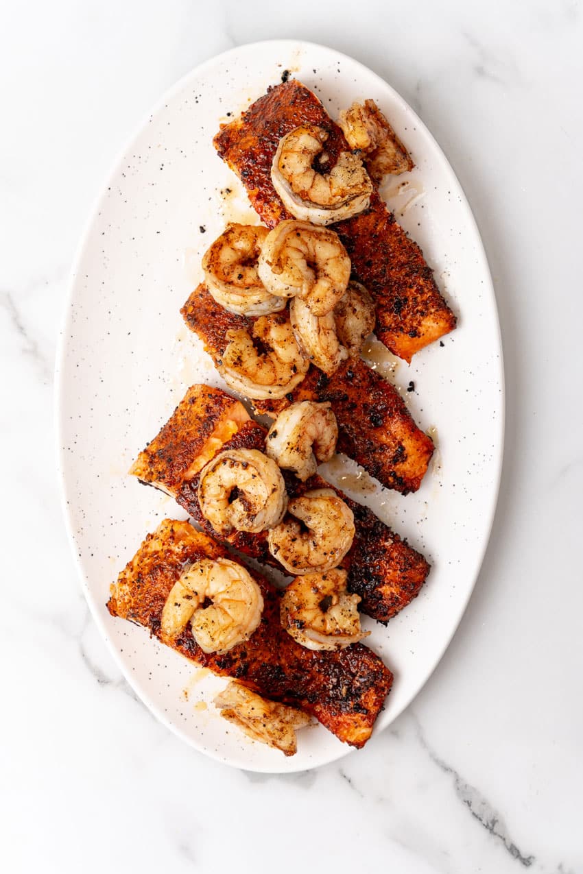 seared salmon filets topped with cooked shrimp on a white serving platter