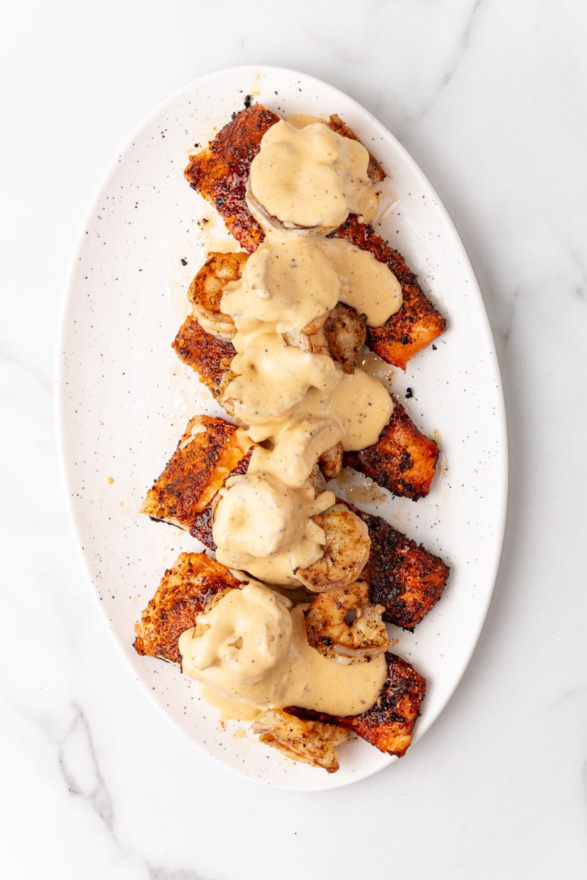 seared salmon filets topped with cooked shrimp drizzled with homemade cream sauce on a white serving platter