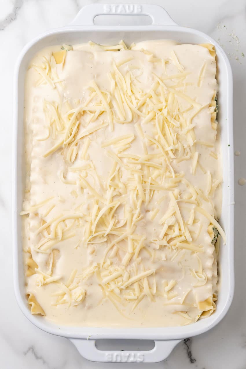 an unbaked white lasagna with spinach in a large white casserole dish