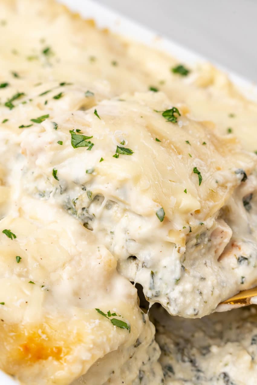 a spatula scooping a slice of spinach artichoke lasagna out of a white baking dish