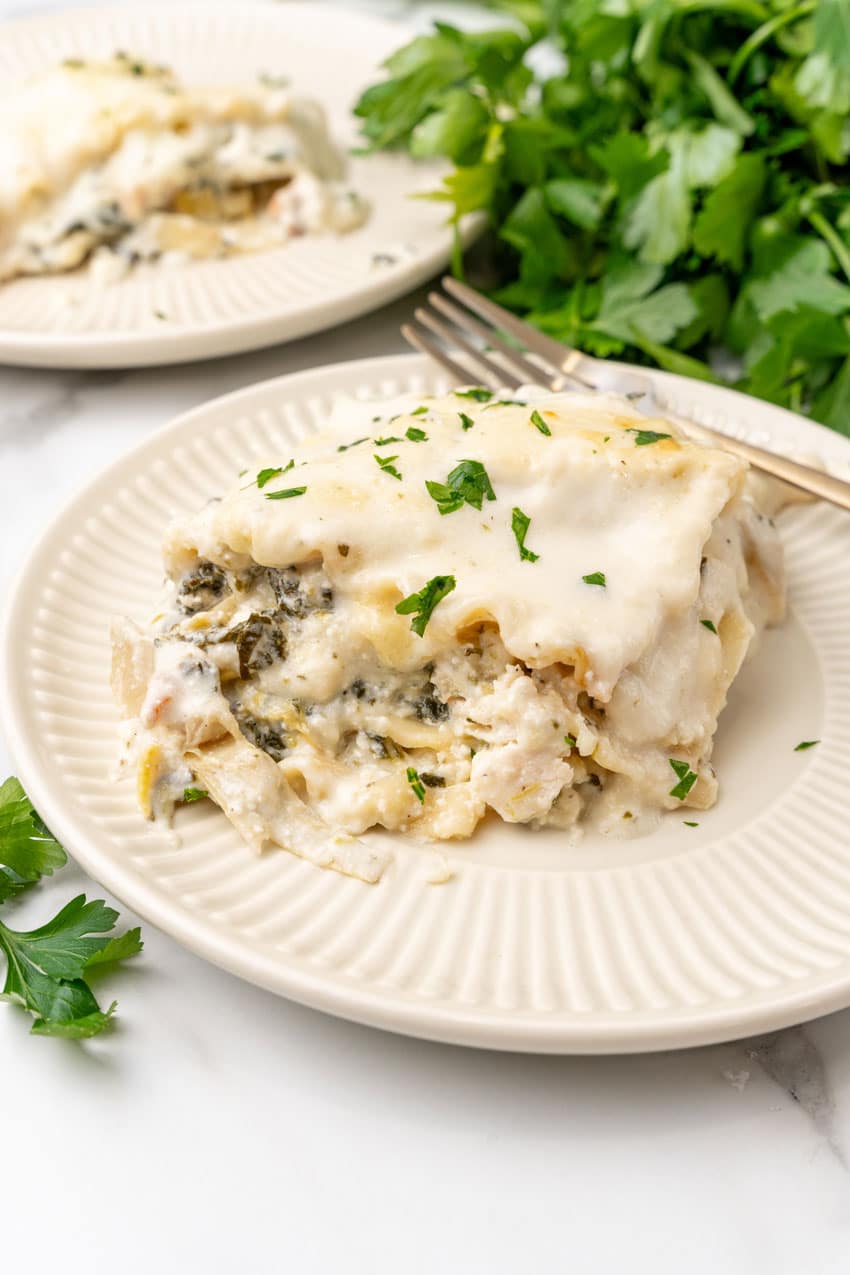 A SLICE OF SPINACH ARTICHOKE LASAGNA ON A SMALL WHITE PLATE