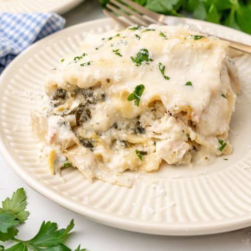 A SLICE OF SPINACH ARTICHOKE LASAGNA ON A SMALL WHITE PLATE