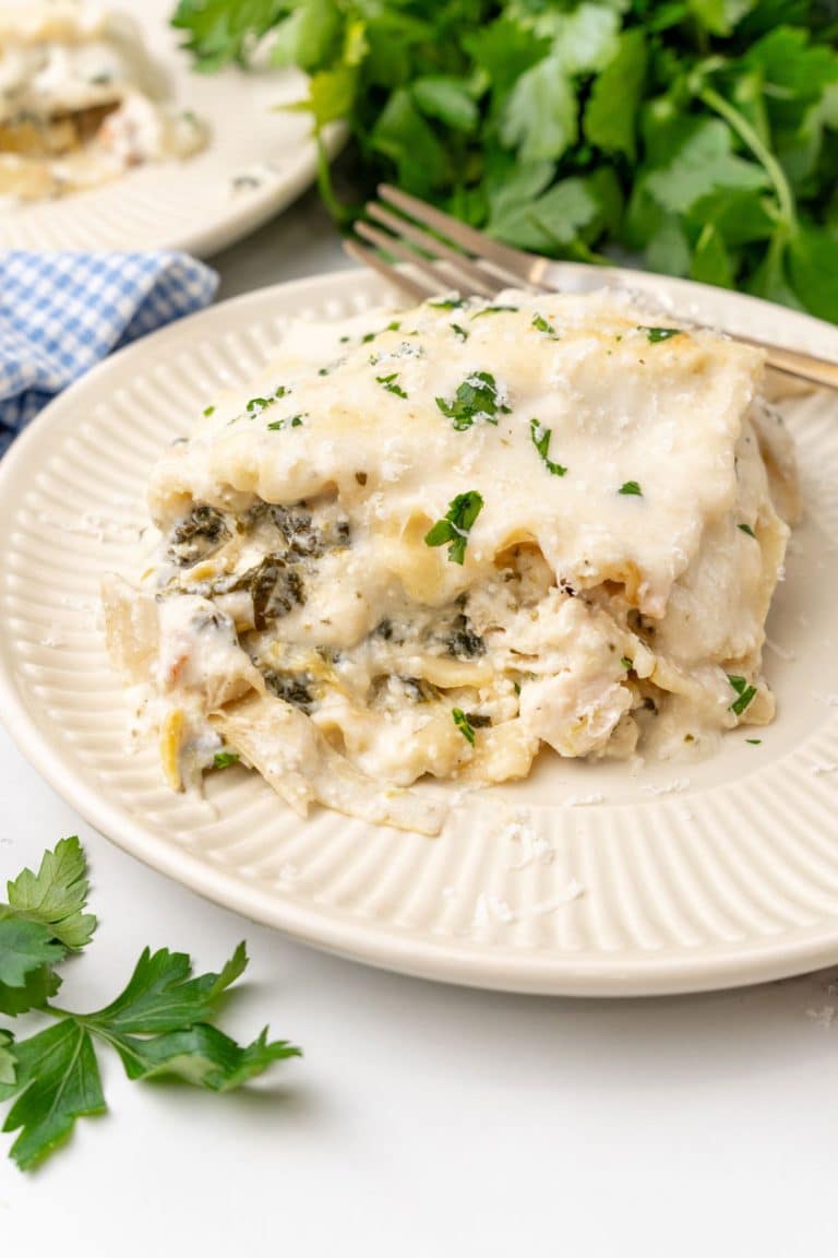 A SLICE OF SPINACH ARTICHOKE LASAGNA ON A SMALL WHITE PLATE