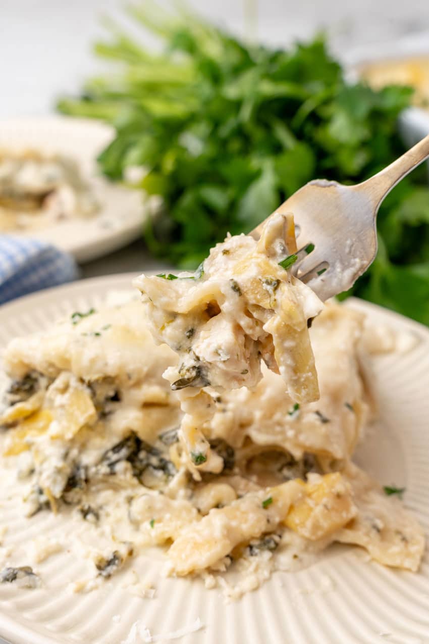 a silver fork holding up a scoop of spinach artichoke lasagna