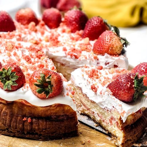 a server removing a slice of strawberry crunch cheesecake from a wooden cutting board