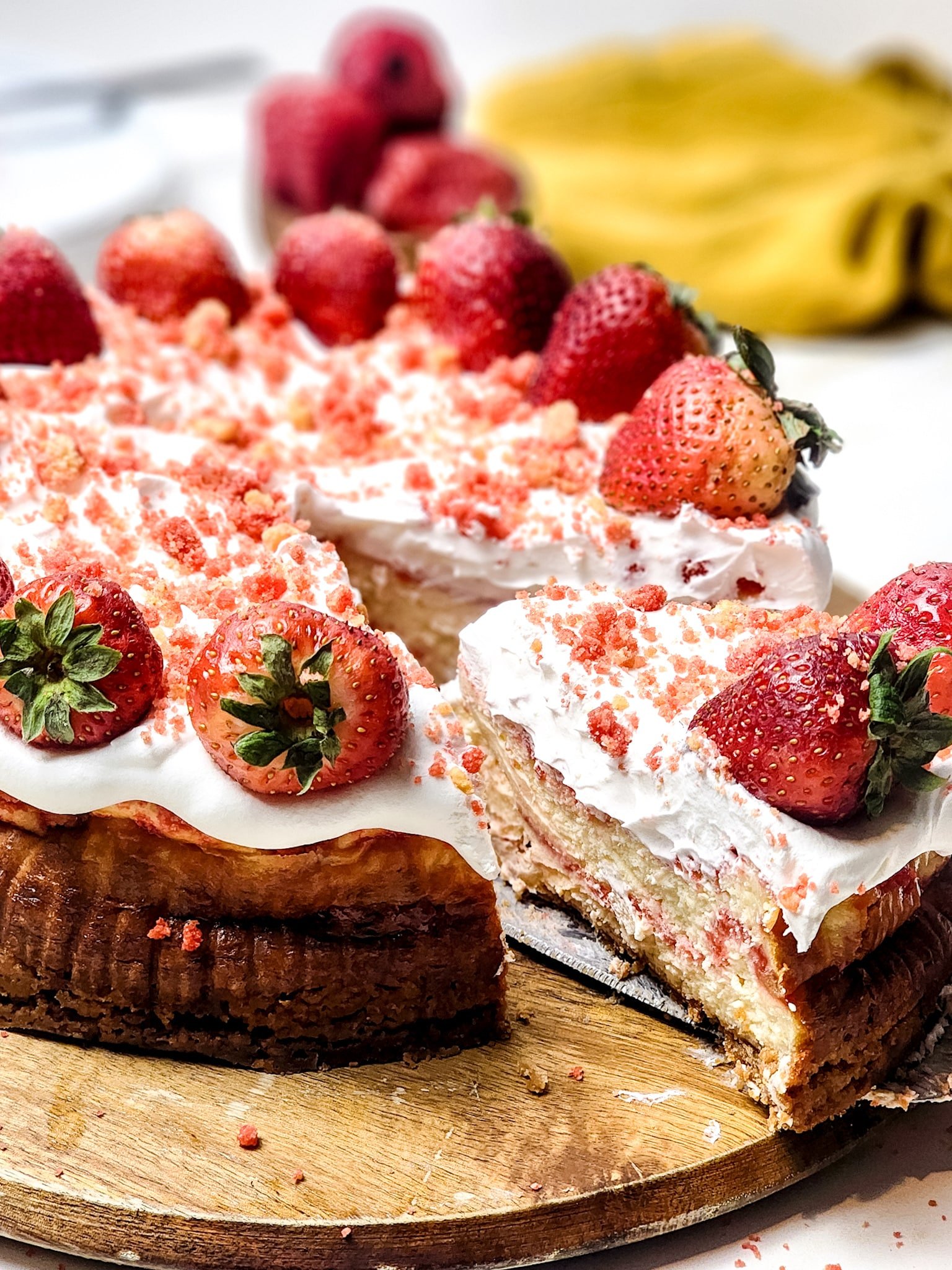 a server removing a slice of strawberry crunch cheesecake from a wooden cutting board