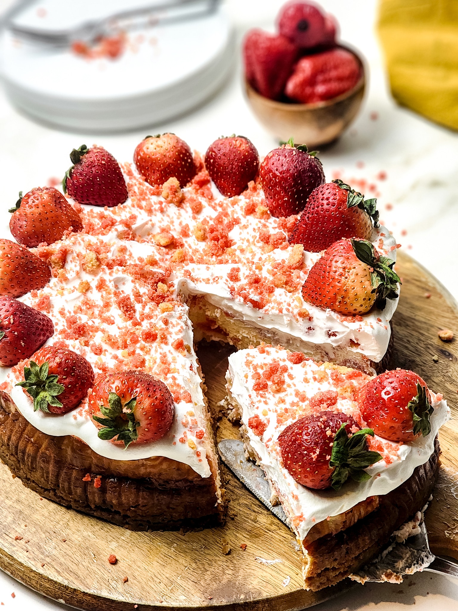 a server removing a slice of strawberry crunch cheesecake from a wooden cutting board