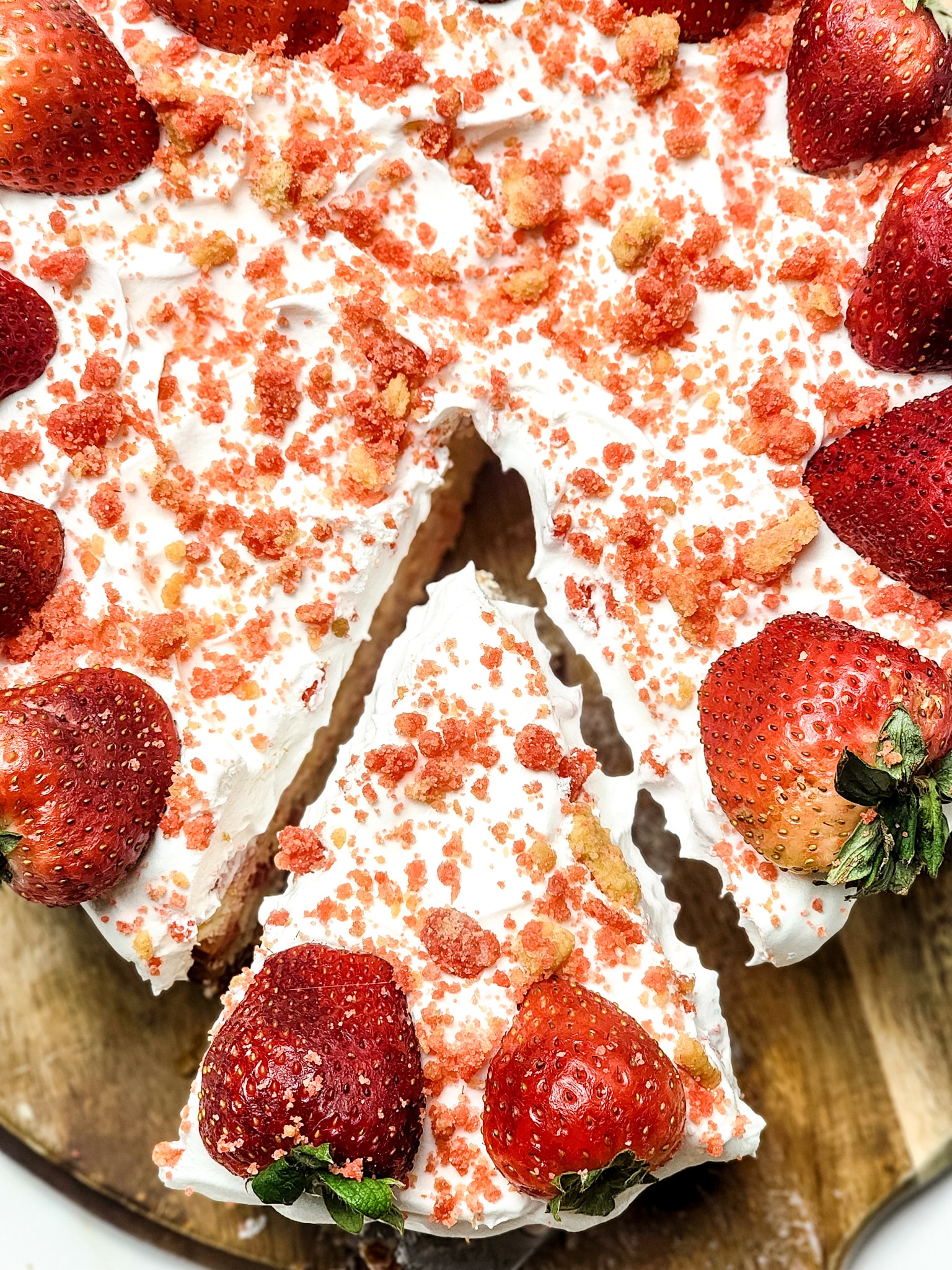 a server removing a slice of strawberry crunch cheesecake from a wooden cutting board