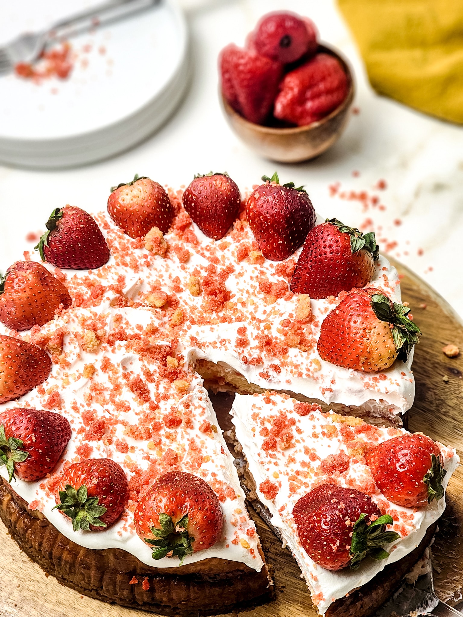 a server removing a slice of strawberry crunch cheesecake from a wooden cutting board