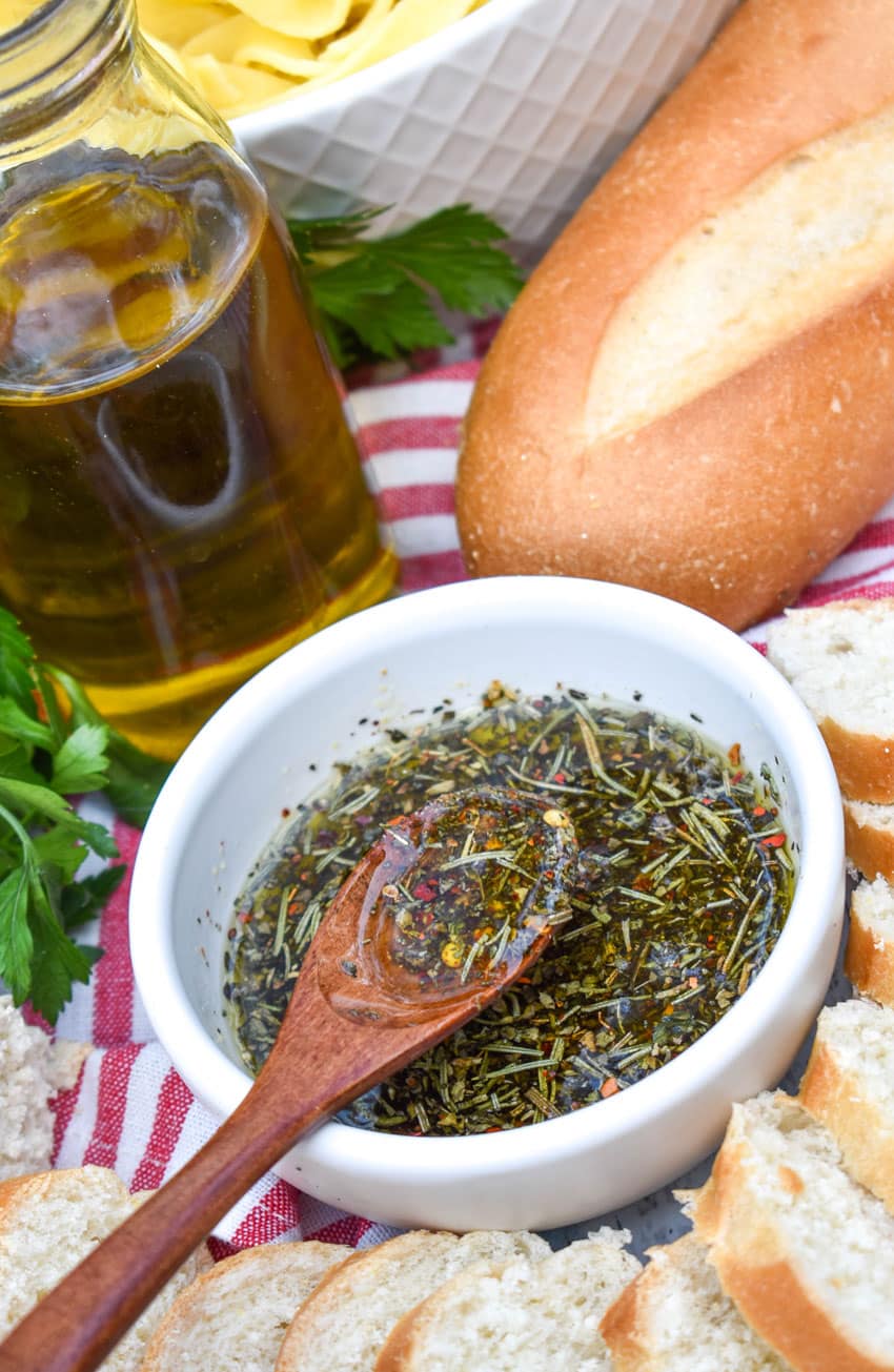 a wooden spoon scooping copycat carrabba's bread dipping oil out of a small white bowl