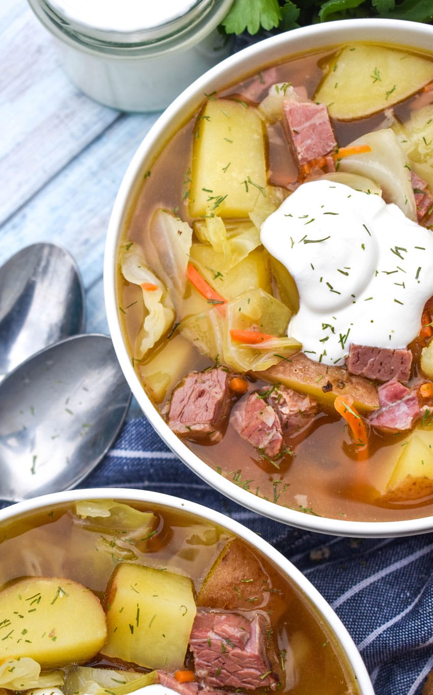 corned beef and cabbage soup topped with sour cream and dill in a white bowl