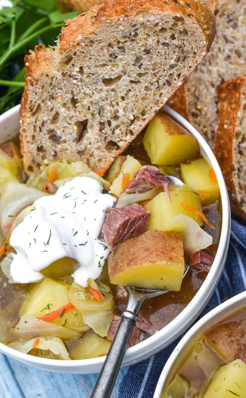 corned beef and cabbage soup topped with sour cream and dill in a white bowl