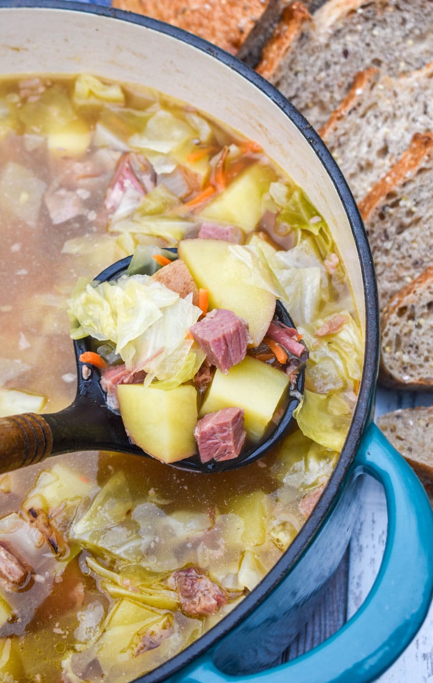 a ladle scooping corned beef and cabbage soup out of a large dutch oven