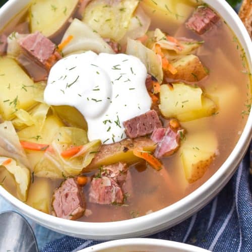 corned beef and cabbage soup topped with sour cream and dill in a white bowl