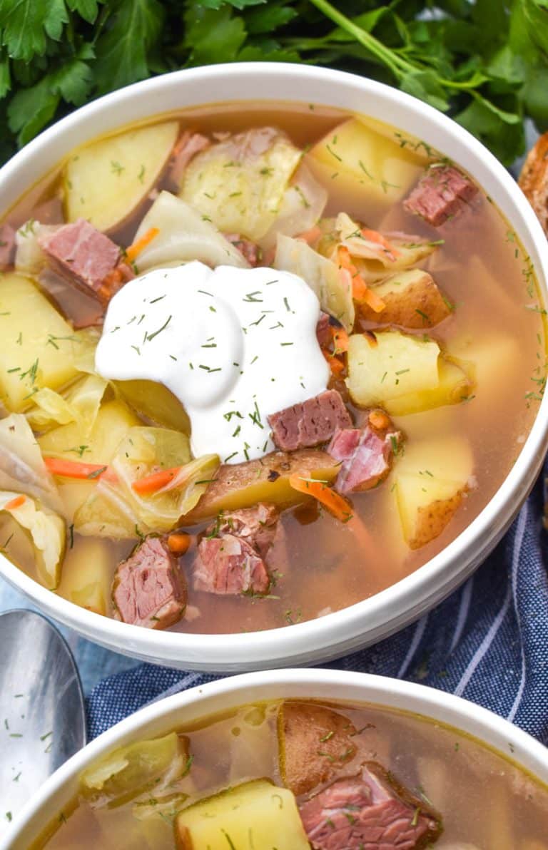 corned beef and cabbage soup topped with sour cream and dill in a white bowl