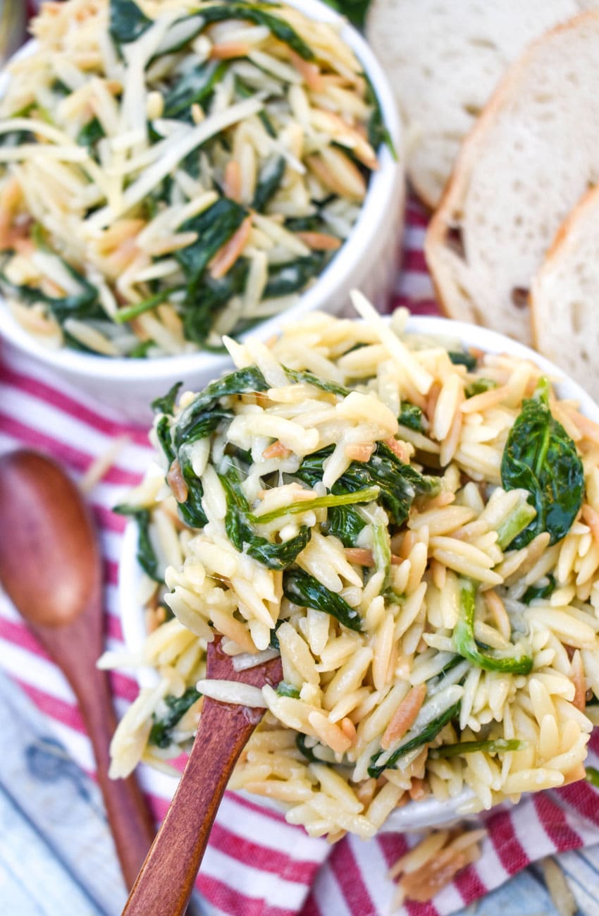 a small wooden spoon scooping spinach parmesan orzo out of a small white ramekin