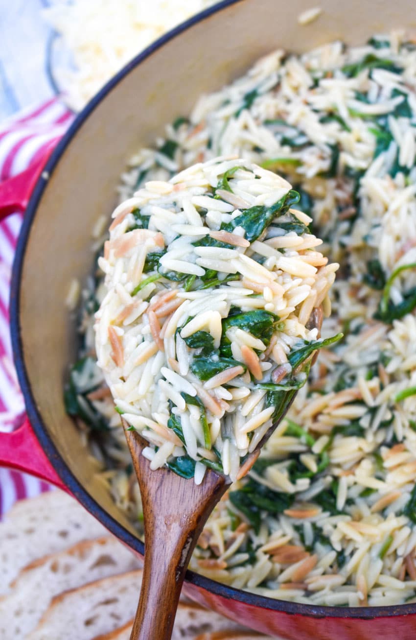 a wooden spoon holding up a scoop of spinach parmesan orzo pasta