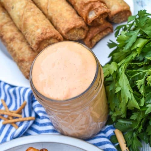 homemade yum yum sauce in a small glass jar with fried egg rolls in the background