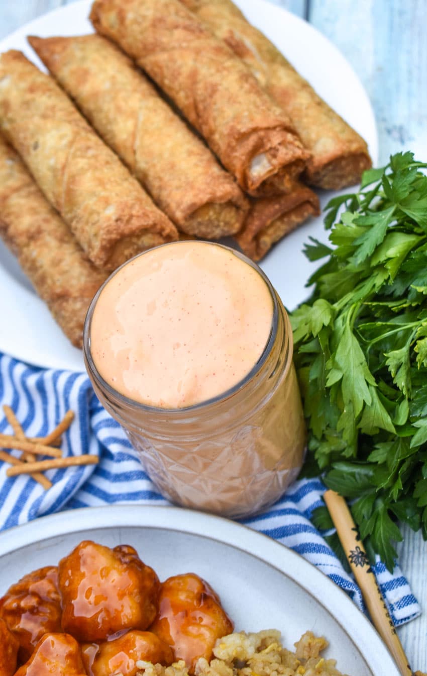 homemade yum yum sauce in a small glass jar with fried egg rolls in the background