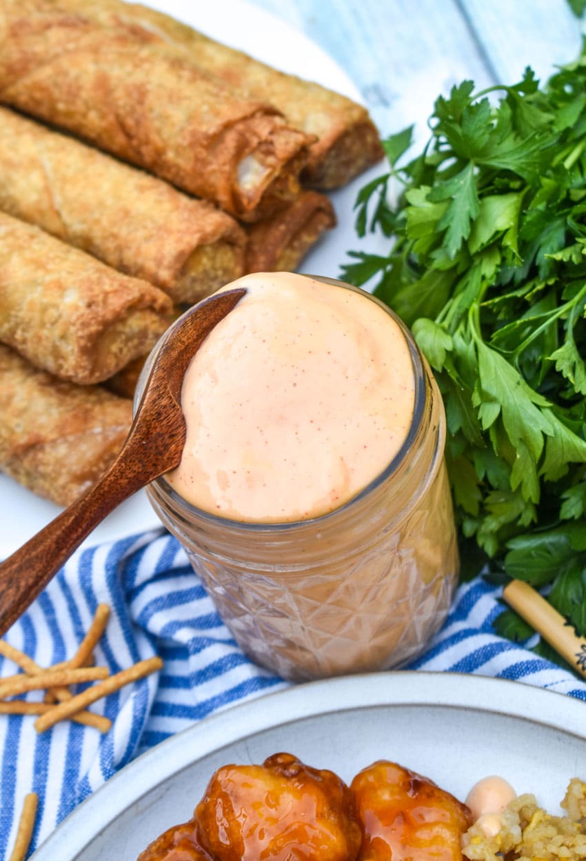 a wooden spoon scooping homemade yum yum sauce out of a small glass jar