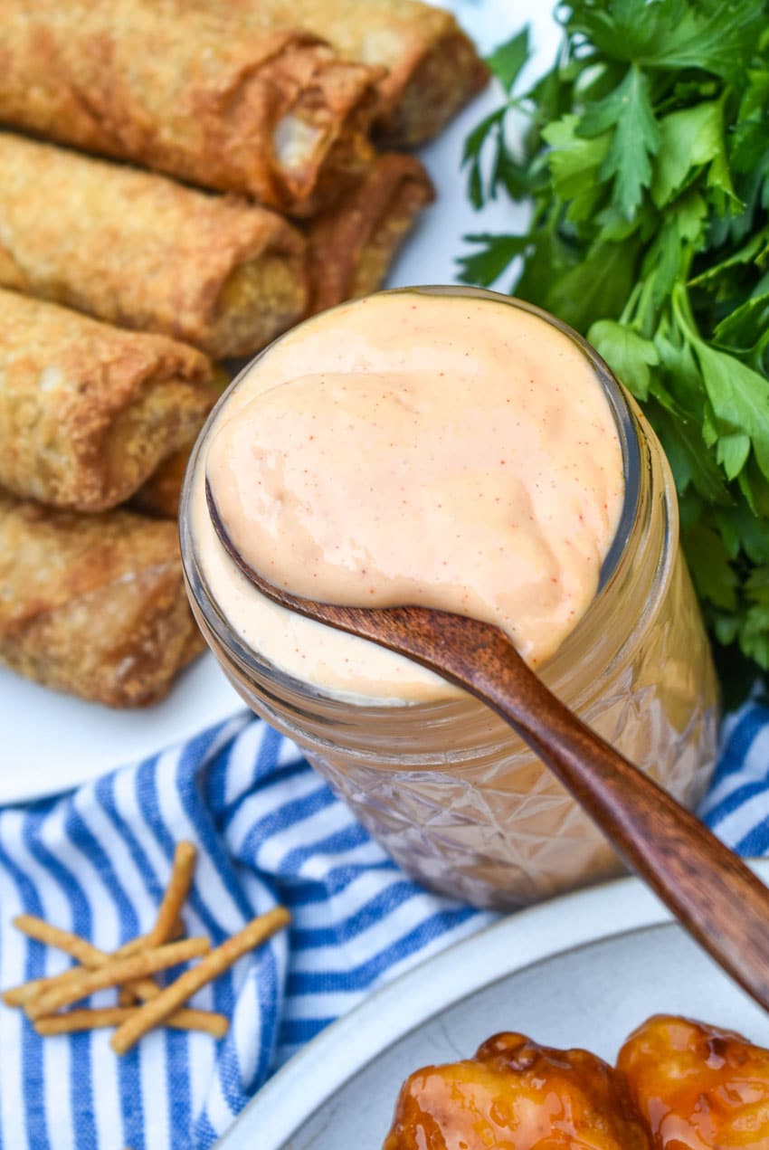 a wooden spoon scooping homemade yum yum sauce out of a small glass jar