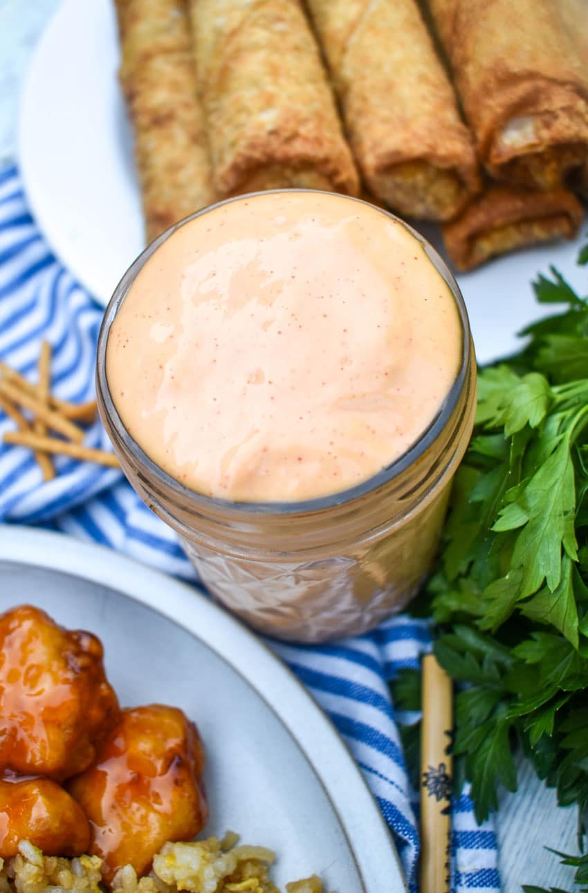 homemade yum yum sauce in a small glass jar with fried egg rolls in the background