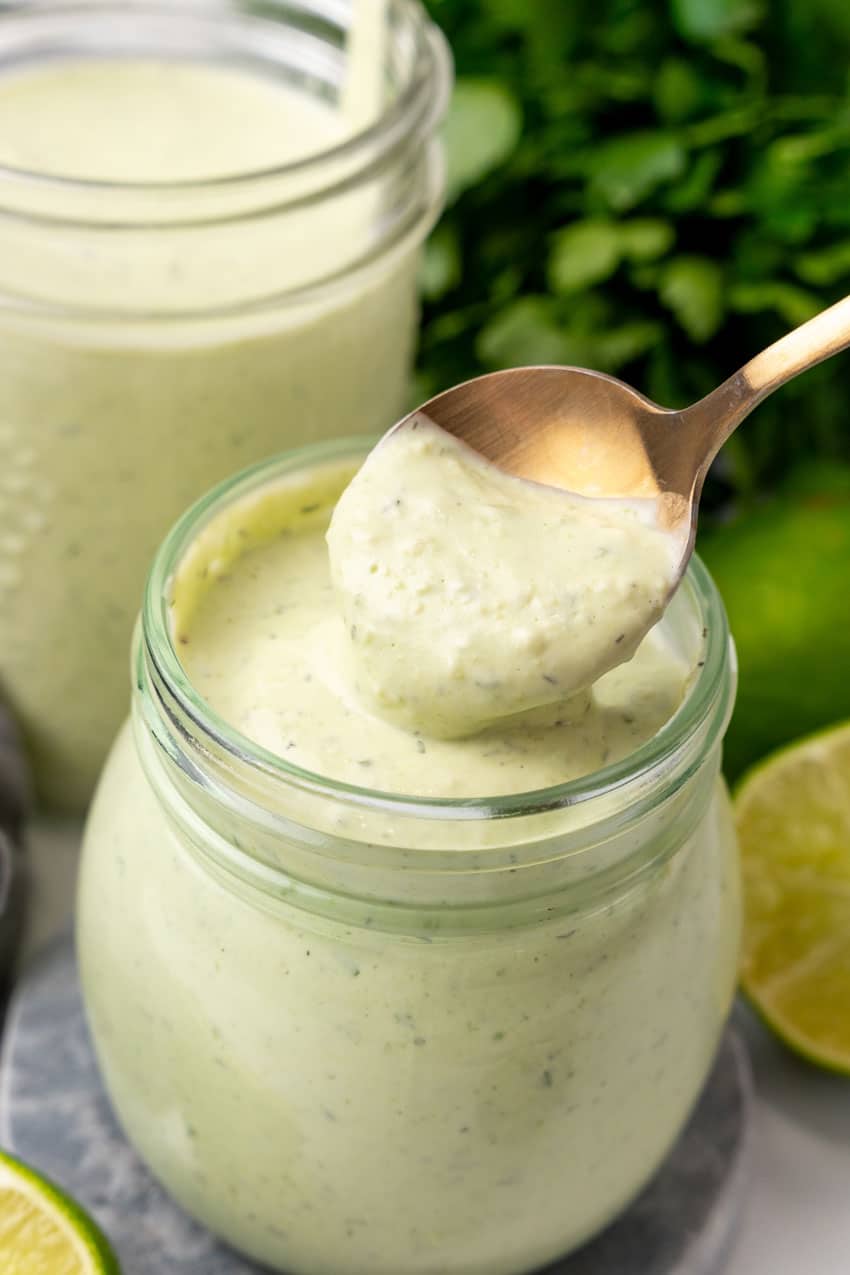 a gold spoon scooping homemade avocado lime dressing out of a small glass jar